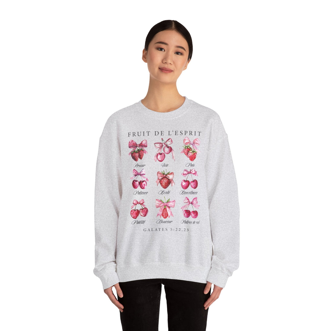 Une femme porte un sweat-shirt gris chiné orné d'illustrations de fruits et de nœuds roses.