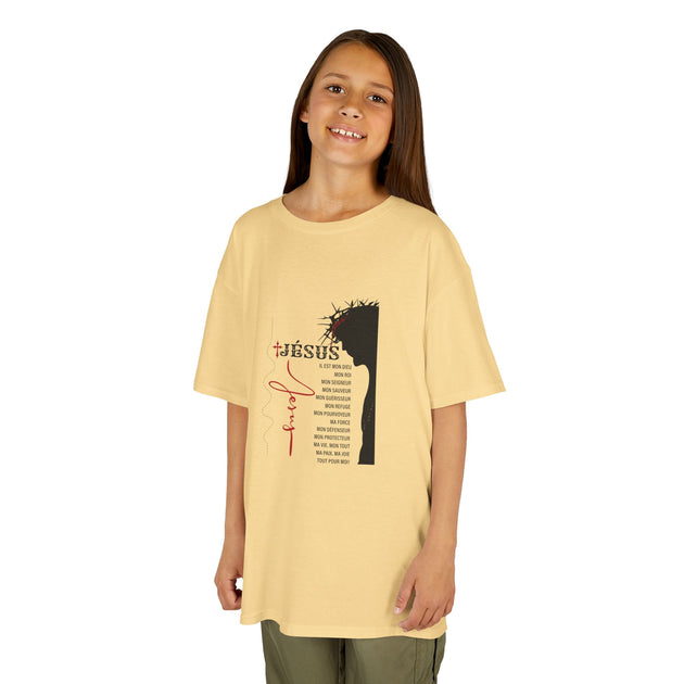 T-shirt beige pour enfant avec une illustration de Jésus et une liste de ses attributs en français.
