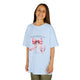 Une enfant porte un t-shirt bleu clair orné d'un ruban rose et du verset Jacques 1:17.