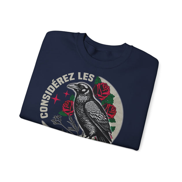 Sweat-shirt bleu marine plié avec une illustration de corbeau, de roses et l'inscription Considérez les.
