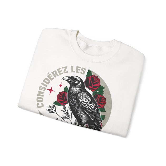 Sweatshirt blanc plié avec une illustration de corbeau, de roses et l'inscription Considérez les.