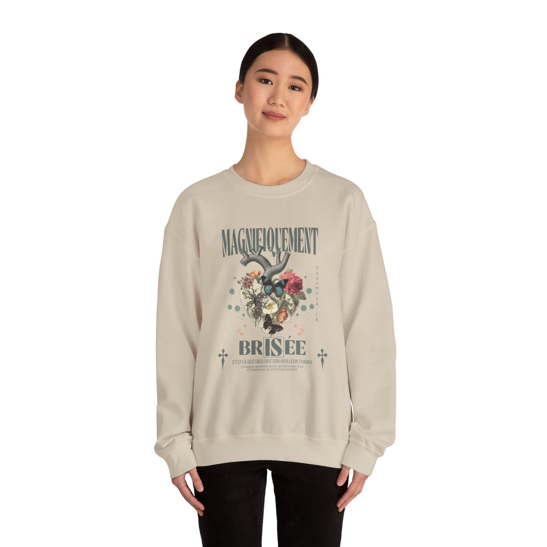Une femme porte un sweat-shirt beige avec un motif de cœur floral et le texte Magnifiquement Brisée.