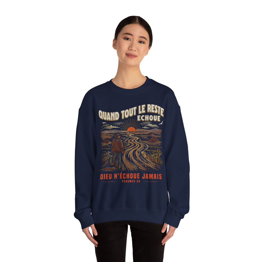 Une femme porte un sweatshirt bleu marine avec une illustration de paysage et un message chrétien.