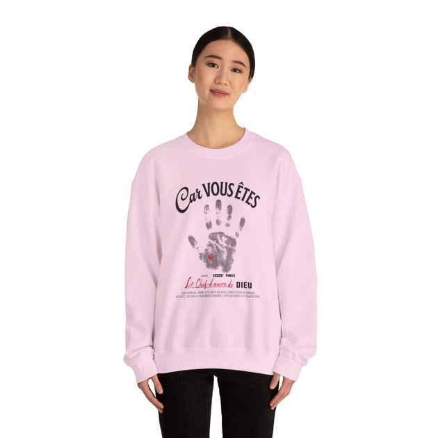 Une femme porte un sweat-shirt rose pâle avec une empreinte de main et un texte religieux.