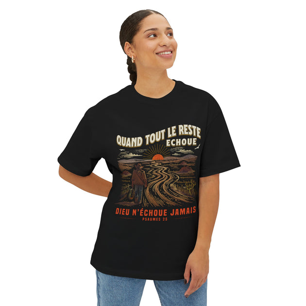 Une femme porte un t-shirt noir oversize illustré d'un voyageur sur un chemin au coucher du soleil.