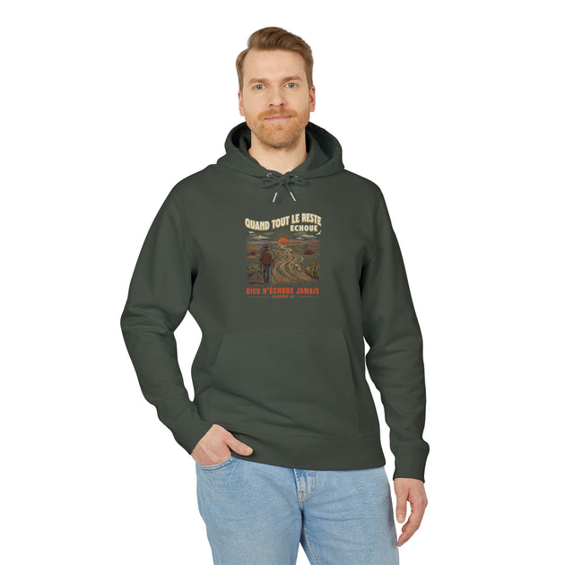 Un homme porte un sweat à capuche vert foncé avec une illustration de paysage et du texte.