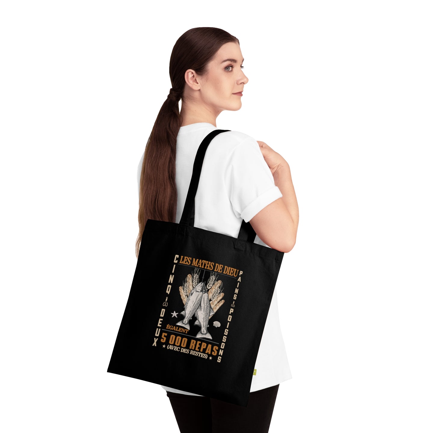 Une femme porte un tote bag noir en coton biologique orné d'une illustration religieuse.