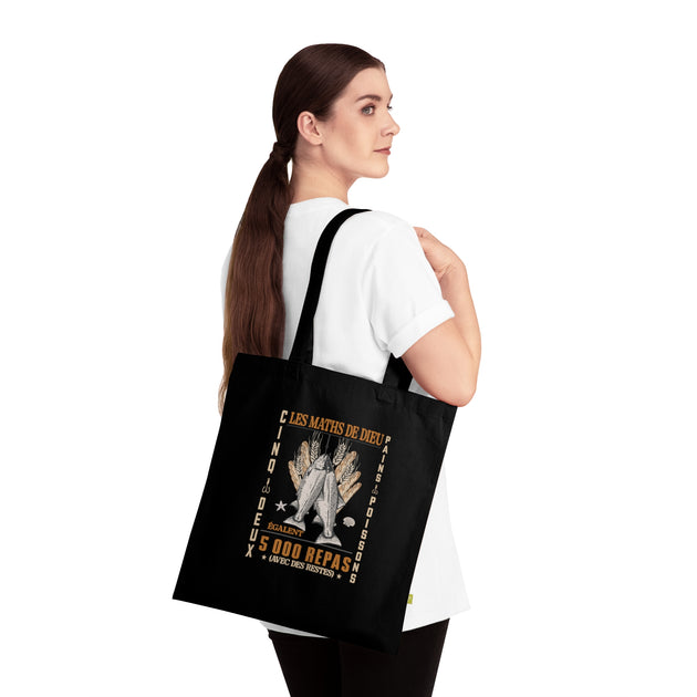Une femme porte un tote bag noir en coton biologique orné d'une illustration religieuse.