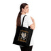 Une femme porte un tote bag noir en coton biologique orné d'une illustration religieuse.