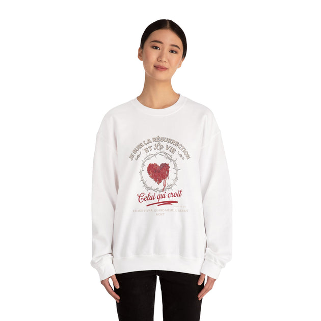 Une femme porte un sweat-shirt blanc avec un motif de cœur couronné d'épines et un texte religieux.