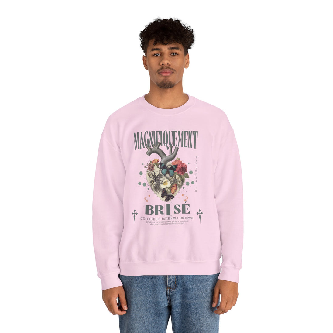 Un homme porte un sweatshirt rose pâle avec une illustration de cœur floral et un texte religieux.