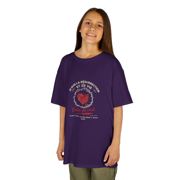 Une jeune fille porte un t-shirt violet avec un motif religieux représentant un cœur et du texte.