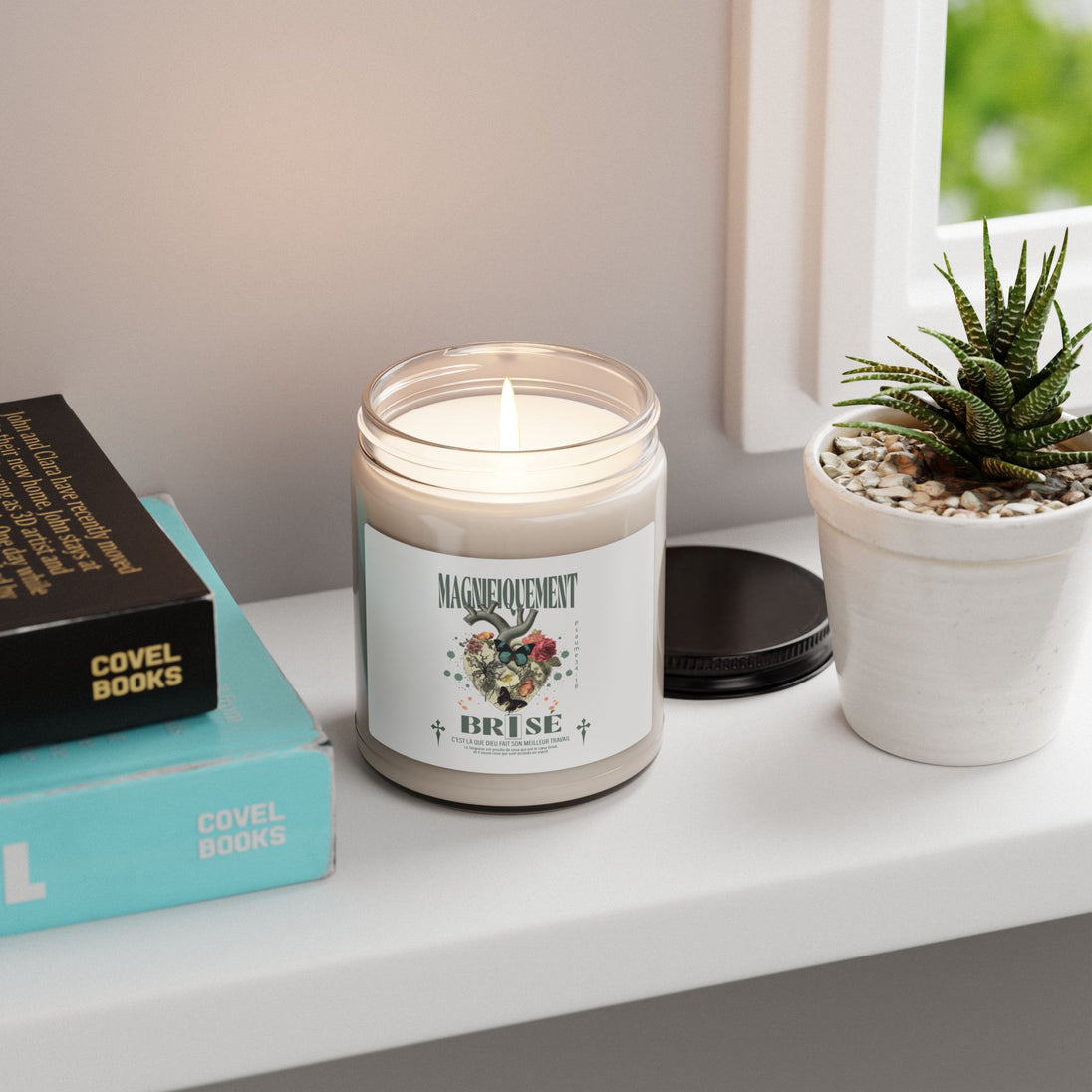 Une bougie allumée dans un pot en verre avec une étiquette illustrée posée près de livres.