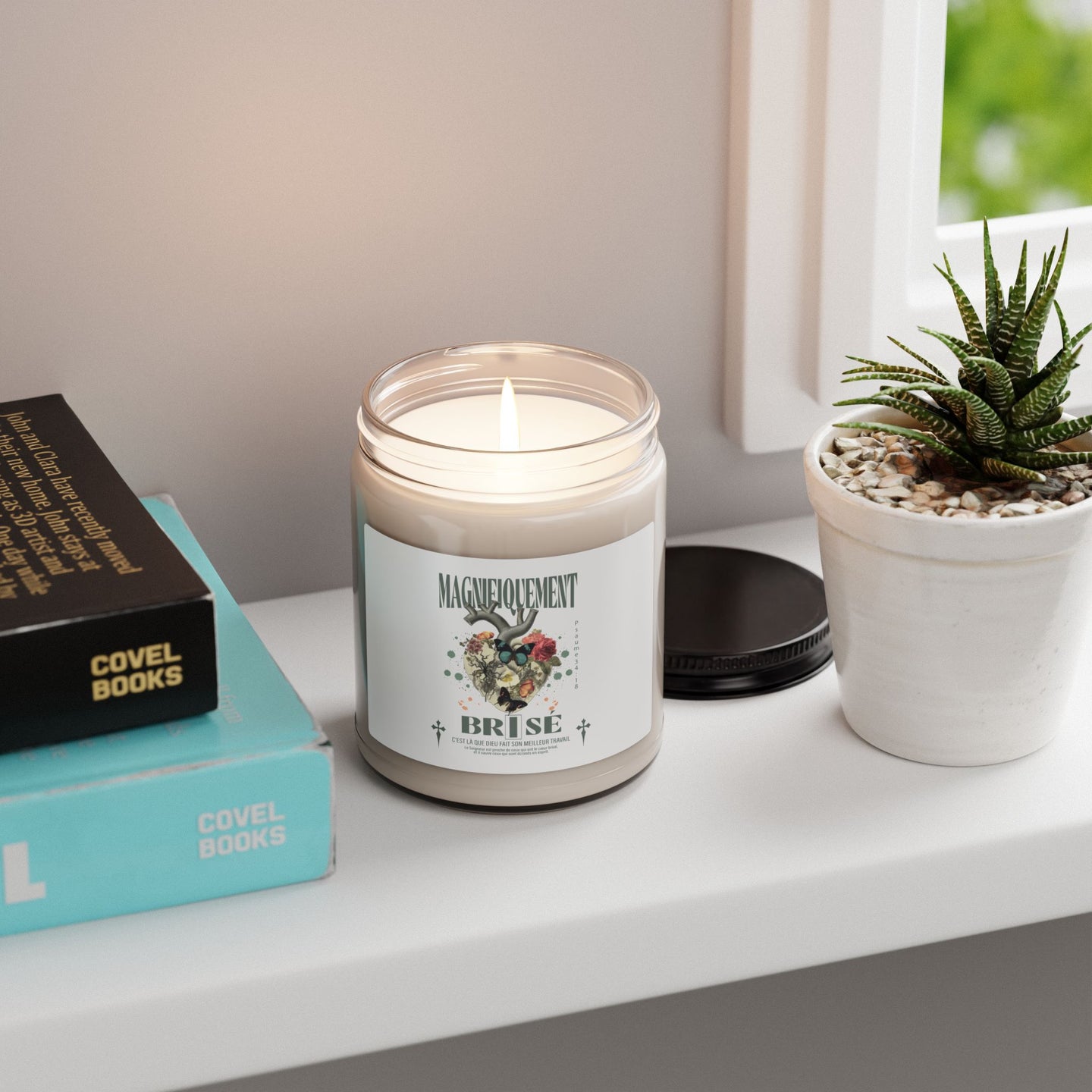 Une bougie allumée dans un pot en verre avec une étiquette illustrée posée près de livres.