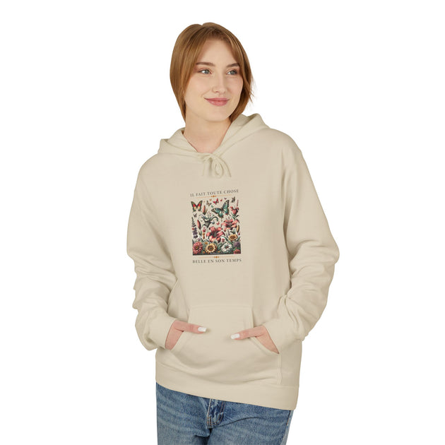 Une femme porte un sweat à capuche beige avec un motif floral et des papillons sur la poitrine.