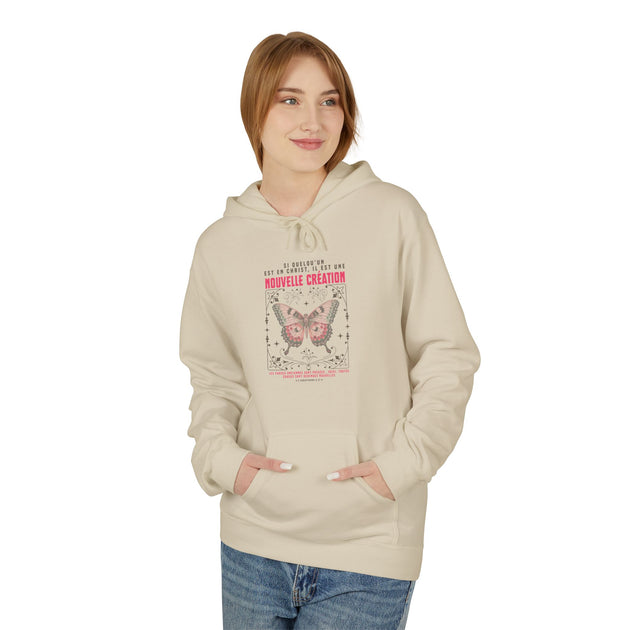 Une femme porte un sweat à capuche beige orné d'un papillon et d'un texte religieux en français.