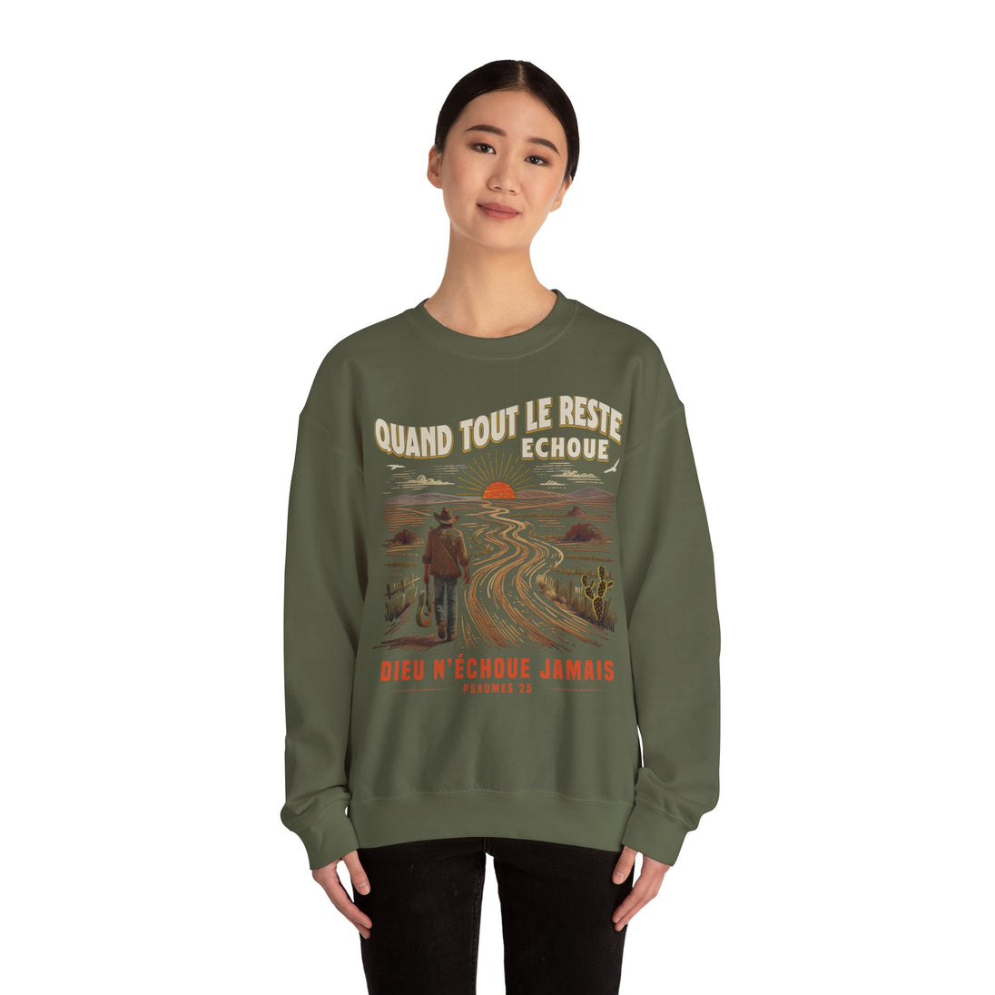 Une femme porte un sweatshirt vert olive avec une illustration de voyageur et un message chrétien.