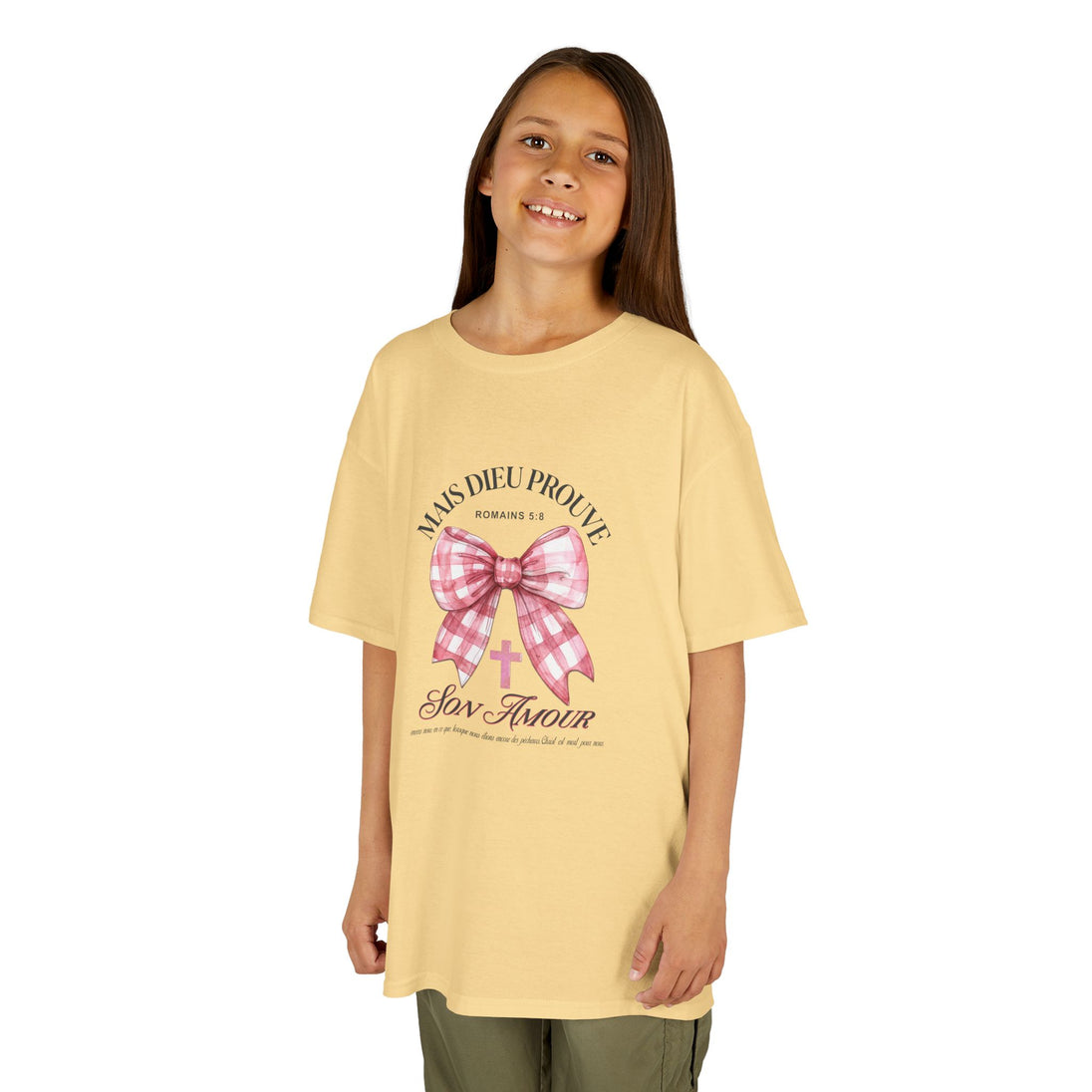 Une jeune fille porte un t-shirt jaune pâle orné d'un nœud rose à carreaux et d'une croix.