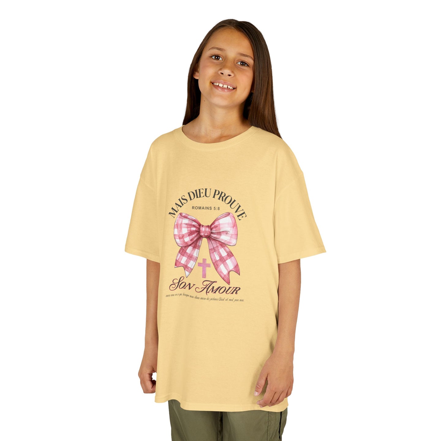Une jeune fille porte un t-shirt jaune pâle orné d'un nœud rose à carreaux et d'une croix.