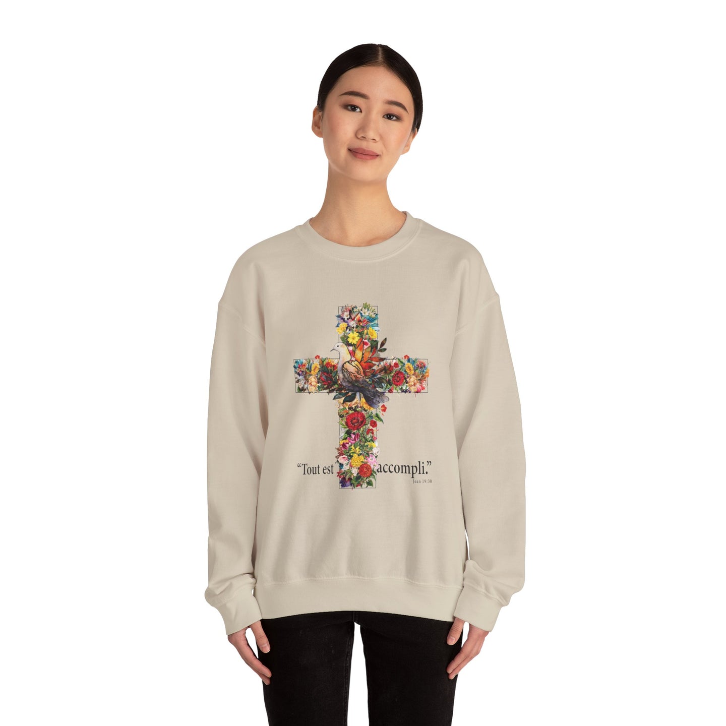 Une femme porte un sweat-shirt beige orné d'une croix florale et de l'inscription Tout est accompli.