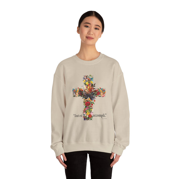 Une femme porte un sweat-shirt beige orné d'une croix florale et de l'inscription Tout est accompli.