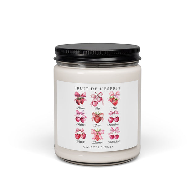 Bougie en cire dans un pot en verre avec une étiquette illustrée de fruits et de rubans roses.