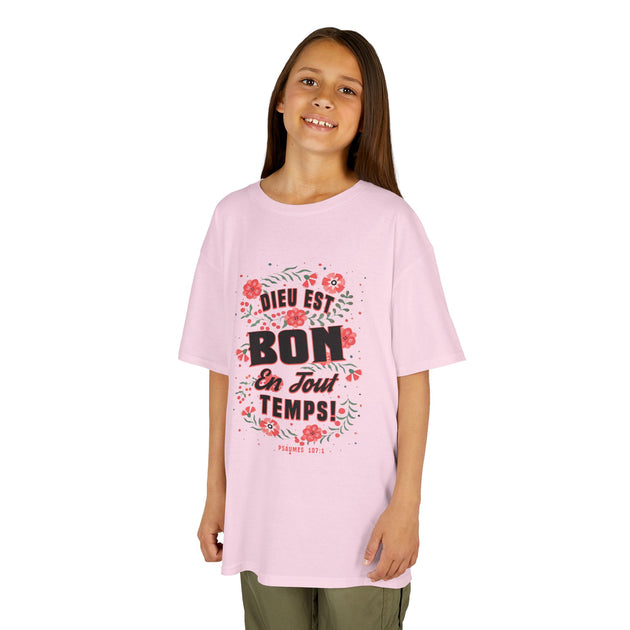 Une jeune fille porte un t-shirt rose orné d'un motif floral et du texte Dieu est bon en tout temps.