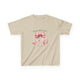 T-shirt beige pour enfant orné d'un ruban rose à l'aquarelle et d'une inscription religieuse.