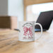 Un mug blanc en céramique orné d'un nœud vichy rose, d'une croix et du verset Romains 5:8.