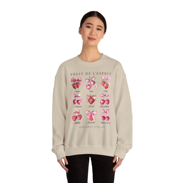 Une femme porte un sweat-shirt beige orné d'illustrations de fruits et de textes bibliques.
