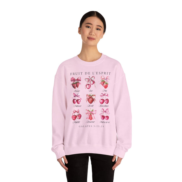Une femme porte un sweat-shirt rose pâle orné d'illustrations de fruits et de textes bibliques.