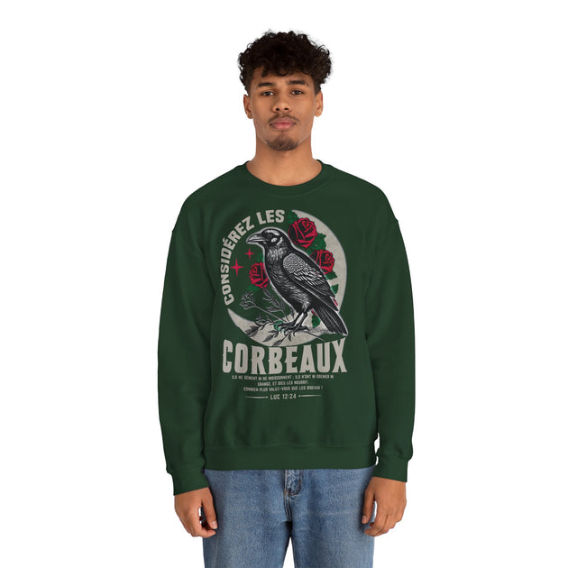 Un homme porte un sweatshirt vert foncé orné d'une illustration de corbeau et de texte en français.