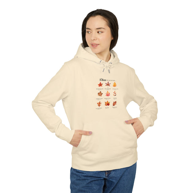 Une femme porte un sweat à capuche beige orné d'un motif de feuilles et de textes bibliques.