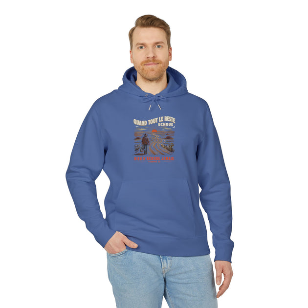 Un homme porte un sweat à capuche bleu avec une illustration de désert et un message religieux.