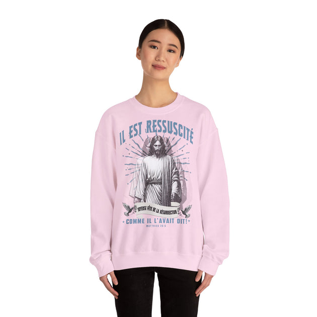 Une femme porte un sweat-shirt rose pâle avec une illustration religieuse et du texte en français.