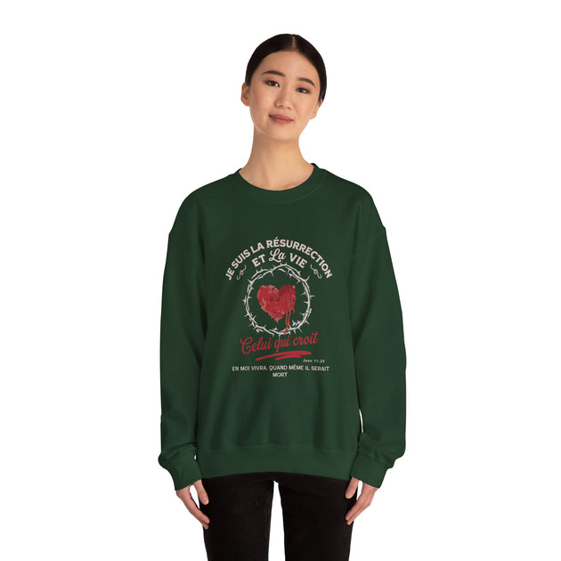 Une femme porte un sweat-shirt vert foncé avec un motif de cœur couronné d'épines et du texte.