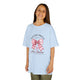 Une jeune fille porte un t-shirt bleu clair avec un motif de nœud rose et une croix chrétienne.