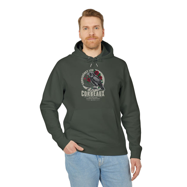Un homme porte un sweat à capuche vert foncé avec une illustration de corbeau et des roses.