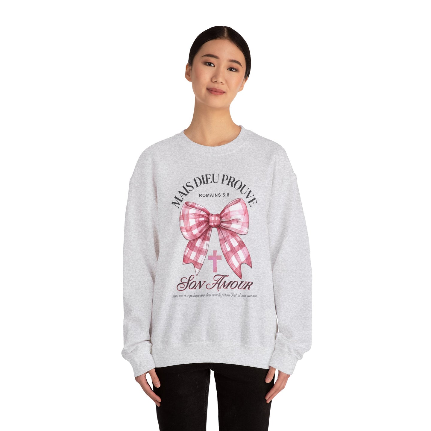 Une femme porte un sweat-shirt gris chiné orné d'un nœud rose à carreaux et d'une croix.