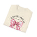 T-shirt beige plié avec un nœud vichy rose et l'inscription Mais Dieu prouve Romains 5:8.