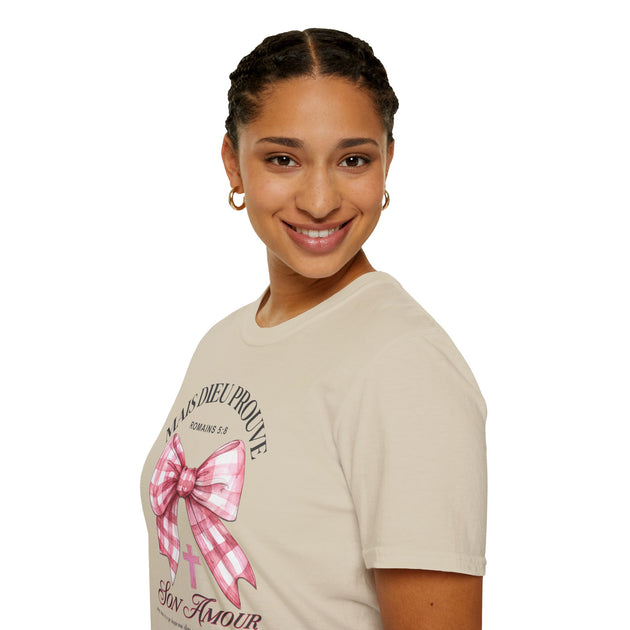 Une femme porte un t-shirt beige avec un motif de nœud vichy rose et une inscription religieuse.