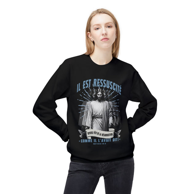 Une femme porte un sweatshirt noir avec une illustration religieuse et le texte Il est ressuscité.