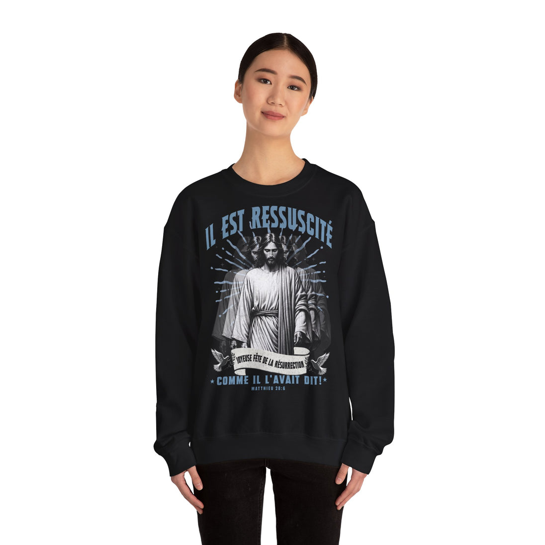 Une femme porte un sweatshirt noir avec une illustration religieuse et le texte Il est ressuscité.