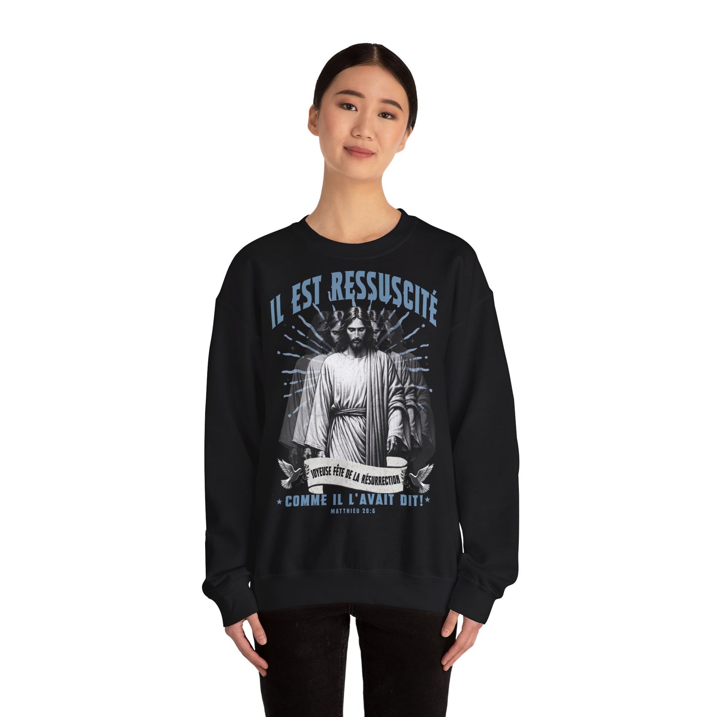 Une femme porte un sweatshirt noir avec une illustration religieuse et le texte Il est ressuscité.