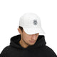 Un homme porte une casquette blanche en coton avec le motif Enracine en Christ brodé sur le devant.