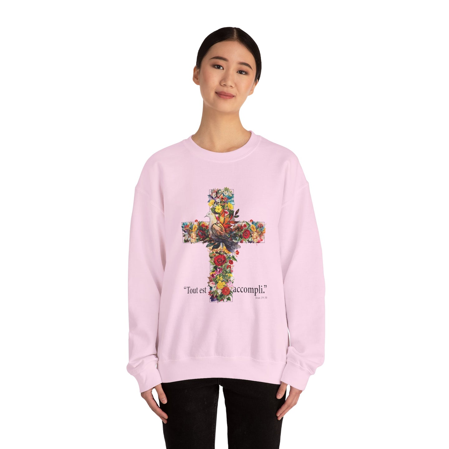 Une femme porte un sweat-shirt rose pâle orné d'une croix florale et de l'inscription Tout est accompli.