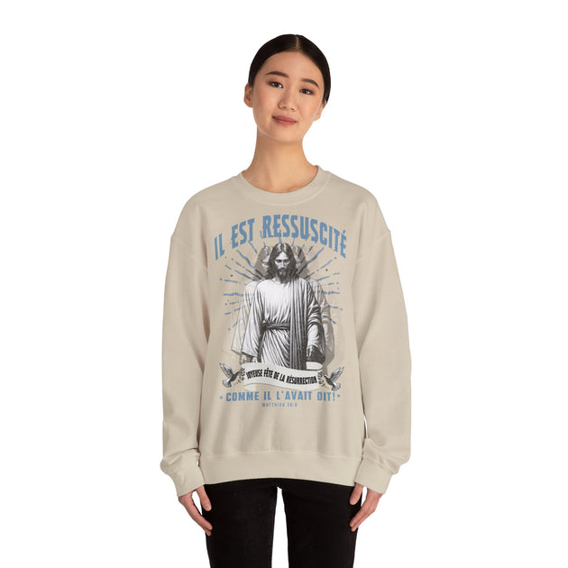 Une femme porte un sweatshirt beige avec une illustration religieuse et le texte Il est ressuscité.