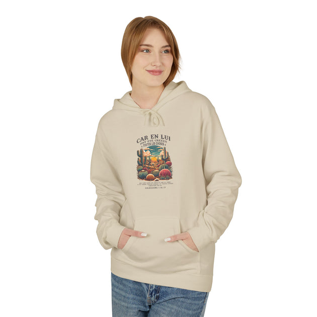 Une femme porte un sweat à capuche beige avec une illustration de cactus et un texte religieux.