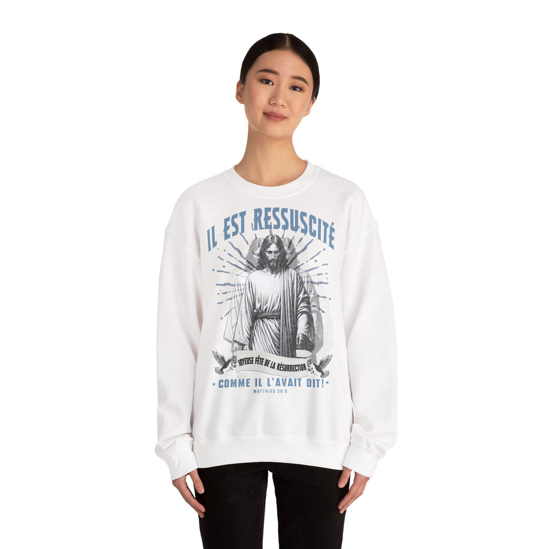 Une femme porte un sweatshirt blanc avec une illustration religieuse et le texte Il est ressuscité.