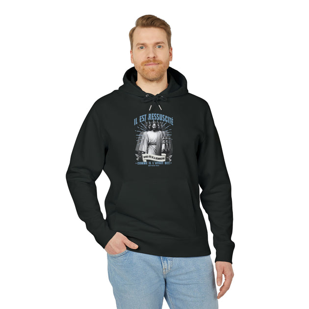 Un homme porte un sweat à capuche noir avec une illustration religieuse et le texte Il est ressuscité.